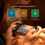Primo piano delle mani che tengono il AYANEO Pocket Micro, che mostra il gioco "Balatro" sullo schermo. Sopra, le icone rappresentano le funzionalità di connettività: WiFi 5 dual-band e BT 5.2, interfaccia USB Type-C e slot per scheda Micro SD, con brevi descrizioni dei vantaggi di ciascuna funzione.