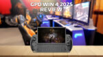 Zdjęcie modelu GPD WIN 4 2025, prezentujące kompaktowe, przenośne urządzenie do gier z fizyczną klawiaturą i zintegrowanymi kontrolerami do gier. Urządzenie jest wyświetlane na drewnianej powierzchni na pierwszym planie, z rozmytą konfiguracją do gier z wieloma monitorami i fotelami do gier w tle. Tekst "GPD WIN 4 2025 REVIEW" jest wyraźnie umieszczony w górnej części obrazu.