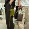 Two individuals wearing AYANEO leather crossbody bags, showcasing the green and brown color options. The bags are worn comfortably, demonstrating their practicality and portability.