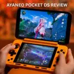 A close-up image for a video review of the AYANEO POCKET DS handheld gaming console. The device, which has a bright orange clamshell design, is held open in two hands. The top screen displays a third-person view of a female anime character in a bright fantasy world, while the smaller, bottom touchscreen displays a darker action scene with glowing effects. Large white text overlaid on the image reads "AYANEO POCKET DS REVIEW." The background is a blurred orange and brown surface.