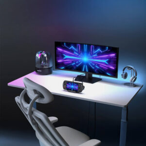 A wide shot of a modern gaming desk setup. A white desk holds a large ultra-wide monitor displaying a vibrant blue and purple abstract design. A GPD WIN 5 handheld gaming console is propped on a stand in front of the monitor, connected by a cable. Other items on the desk include a futuristic speaker, a headphone stand with white headphones, and a chair. The entire scene is lit with purple and blue LED lighting.
