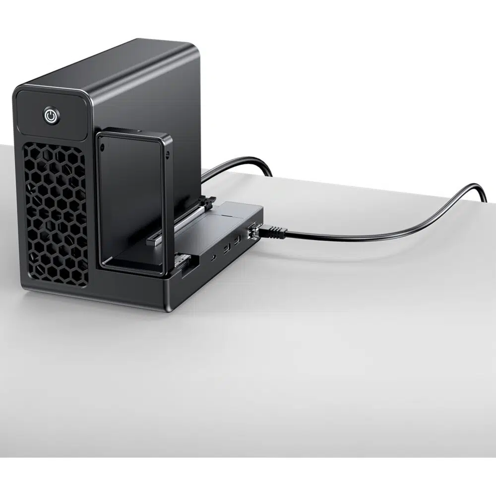 Black desktop NAS/enclosure with a pull-out drive bay and front hexagonal vent, power button, and a cable connected on a white desk surface.